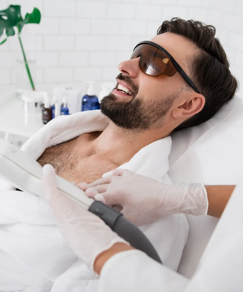 Bearded man wearing laser safety goggles during a hair removal session at a clinic