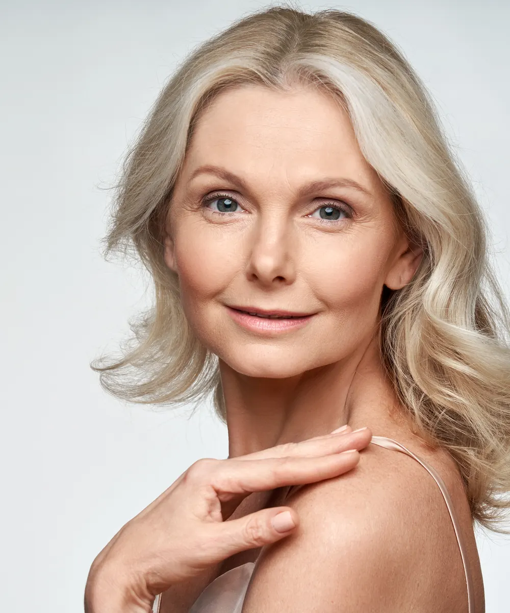 Woman with softly lifted mid face contours resting her hand on her shoulder