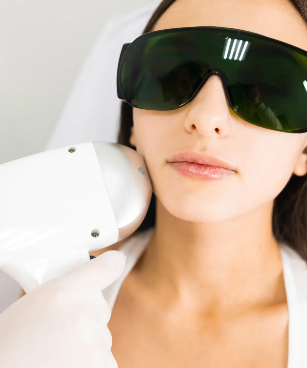 Woman wearing dark protective eyewear as a white handpiece touches her cheek
