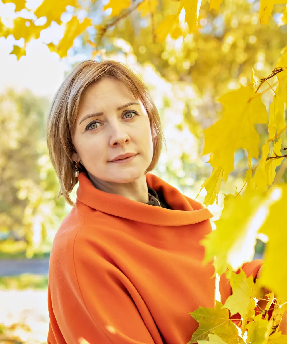 Woman in an orange shawl stands among bright yellow autumn maple leaves