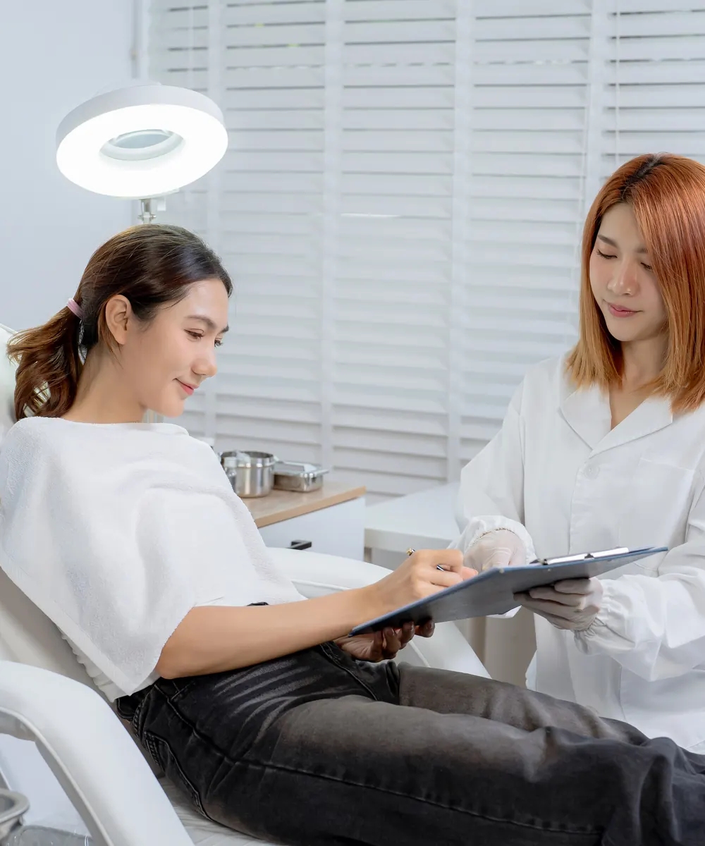 Clinician in a white coat reviews a clipboard with a reclining woman in a treatment chair