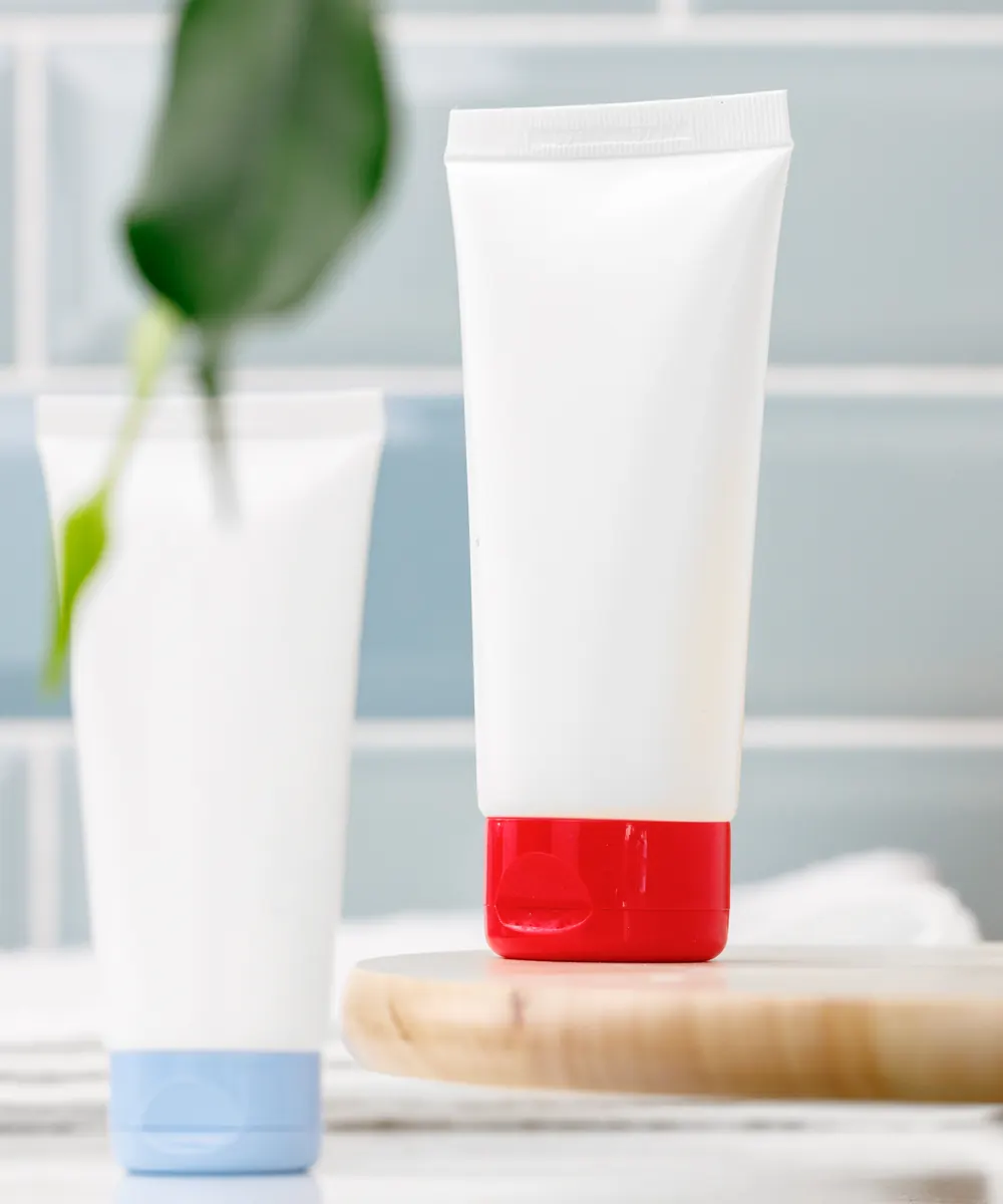 Two plain white skincare tubes on a wooden tray beside a tiled bathroom wall