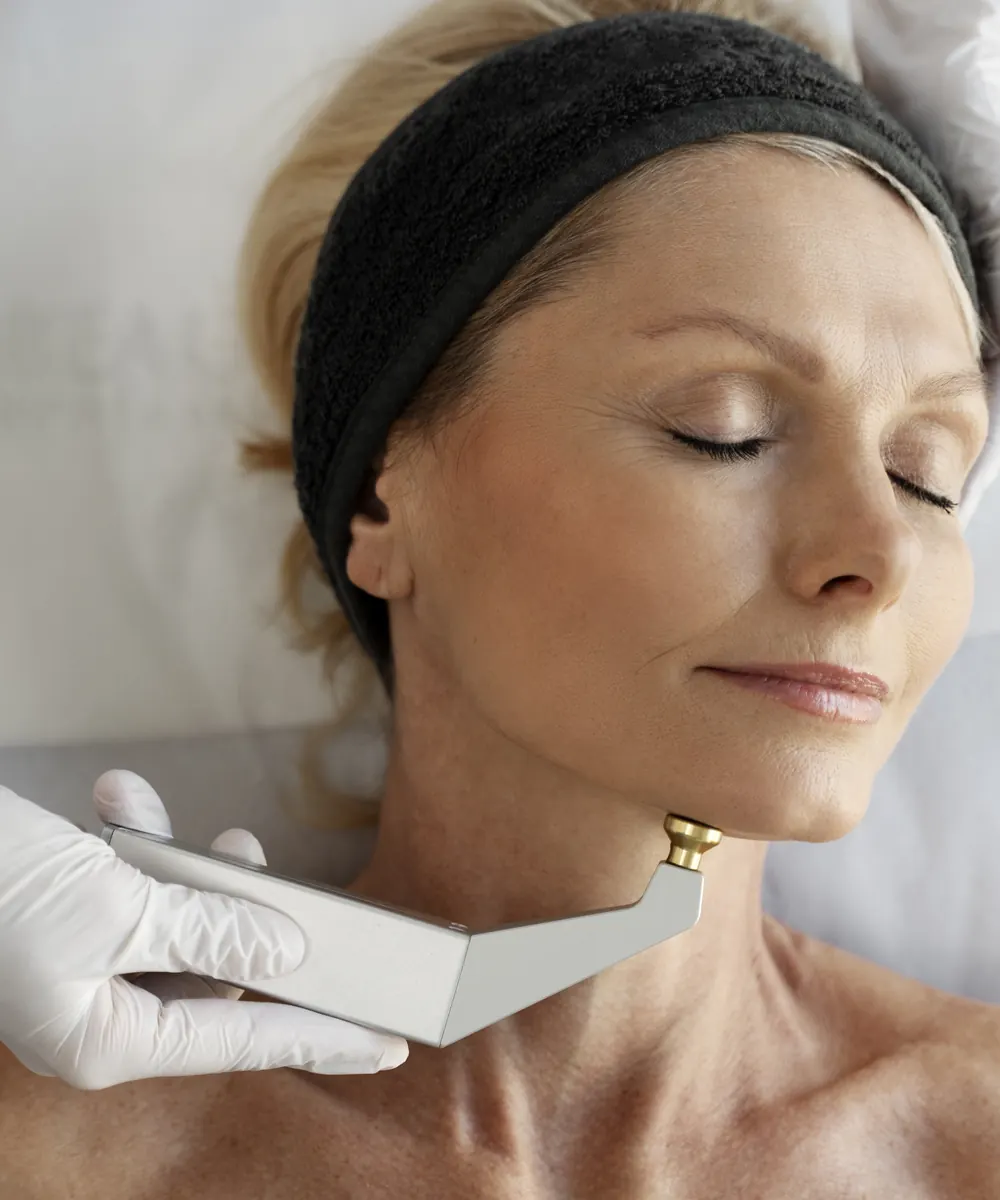 Woman with a black headband rests as a gloved hand holds a device along her jaw