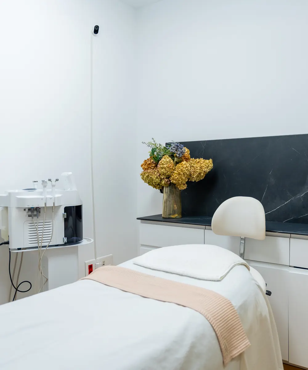 Tidy treatment room with a made up bed, dried flowers and a dark stone wall