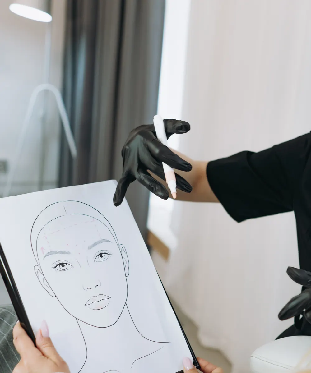 Gloved clinician points to a face sketch held up by a client during consultation