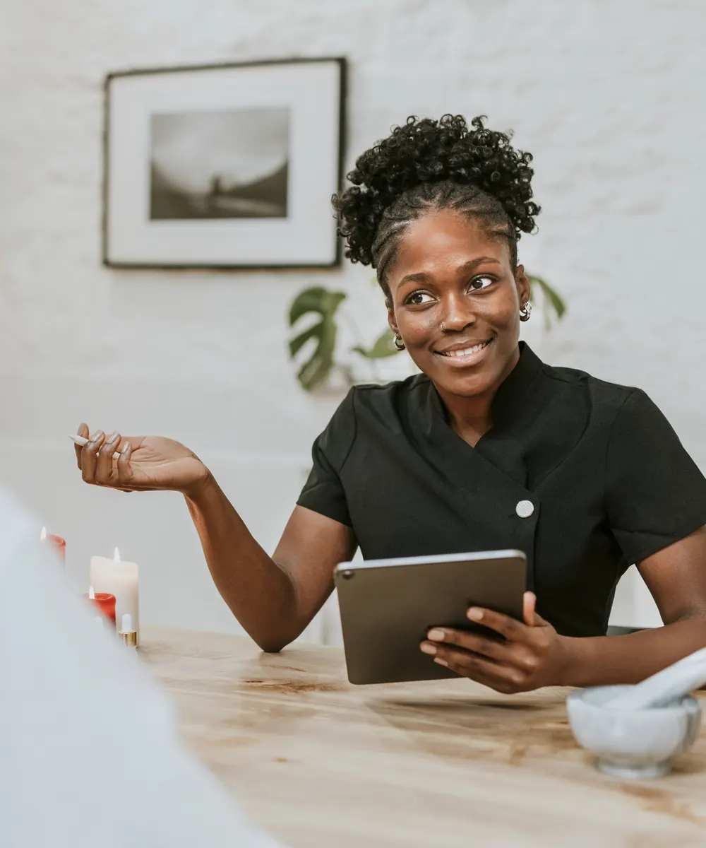 Smiling provider holding a tablet explains a treatment plan to a seated client