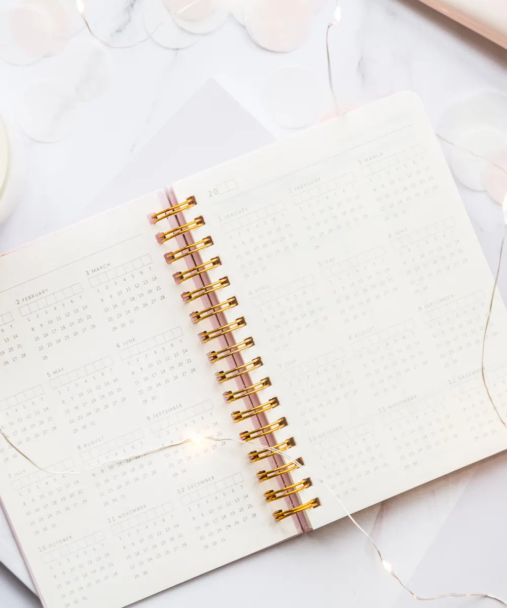 Open spiral bound year calendar on a white desk beside a candle and cotton stems