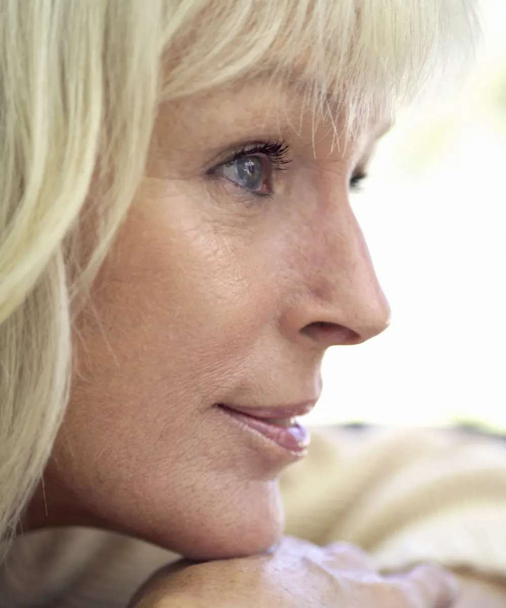 Close profile of a mature woman with blonde hair resting her chin on her hand