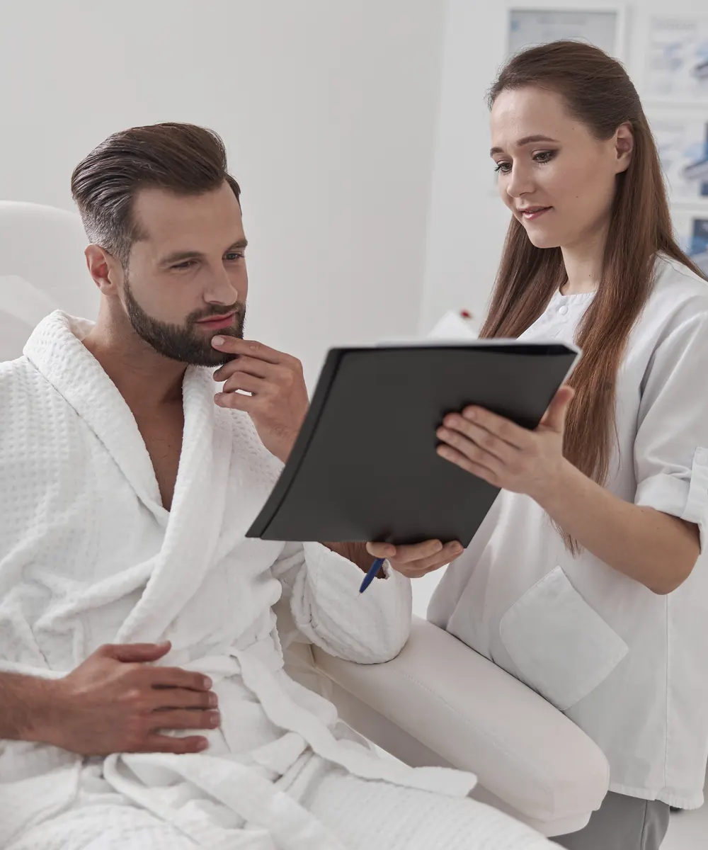 Man in a white robe reviews a folder held by a clinician dressed in white