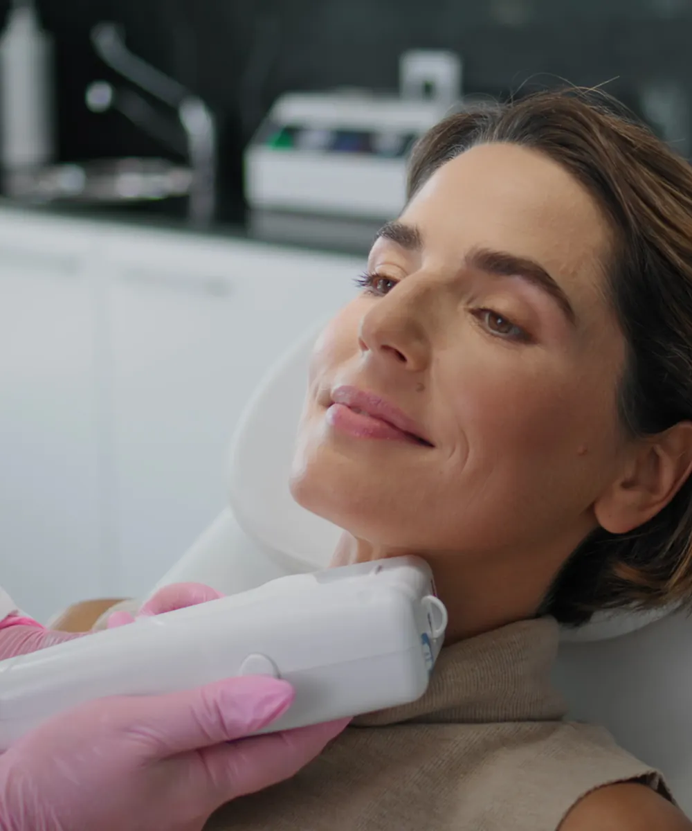 Relaxed woman in a treatment chair as a gloved hand glides a device under her jaw